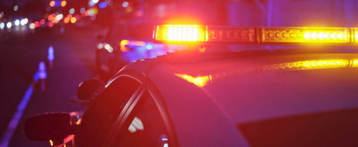 A police car at night alongside a road with emergency lights flashing.